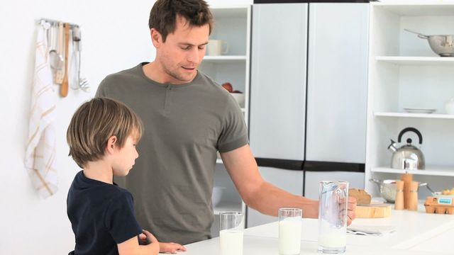 Father pouring milk for his son in a stylish kitchen setting emphasizes family bonding and nutrition. This image is ideal for family-oriented advertising, parenting articles, or promotions about health and lifestyle.