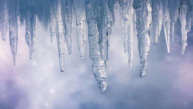 Hanging icicles glistening with melting droplets against pastel winter bokeh backdrop