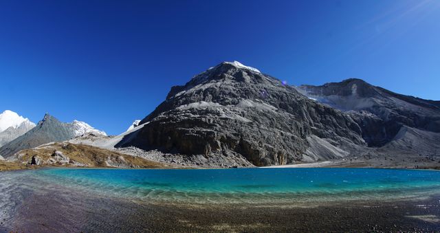 Stunning panoramic view of a turquoise lake with surrounding majestic mountains under a clear blue sky. Perfect for promoting travel destinations, outdoor adventures, nature retreats, and landscape photography. Useful for websites, brochures, and social media posts focused on wilderness and exploration.