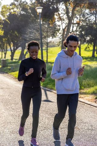 Diverse young adults jogging in sunny park wearing fitness trackers and casual activewear