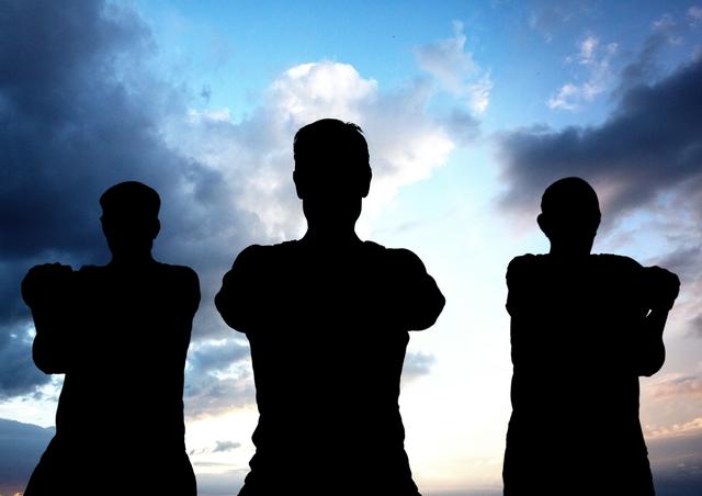 Silhouette of three determined people standing against blue cloudy sky