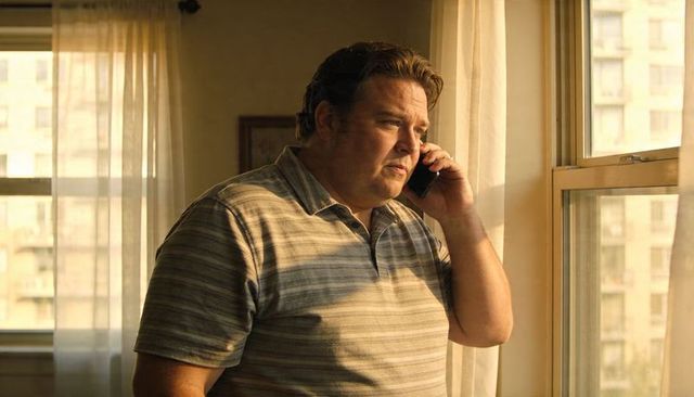 Pensive middle-aged man talking on phone by sunlit apartment window during golden hour, urban interi