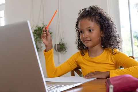 Young girl studying on laptop at home raising pencil doing remote learning and homework