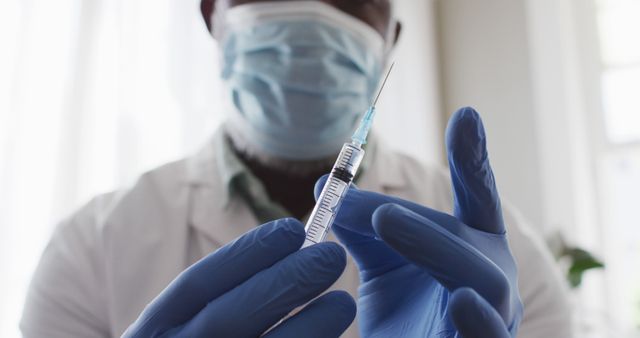 Image features a healthcare professional wearing medical gloves and a mask, preparing a vaccine injection with a syringe. This can be used in articles and content about vaccinations, healthcare services, medical preparations, COVID-19, and immunization programs.