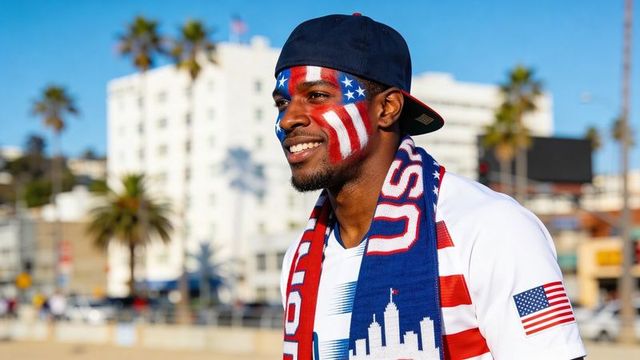 Smiling fan wearing usa scarf and flag face paint on sunny boardwalk with palm trees