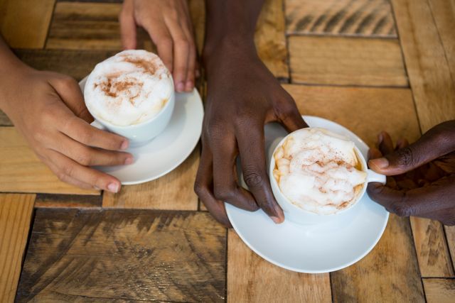High angle close-up of couple hands holding coffee cups in cafe