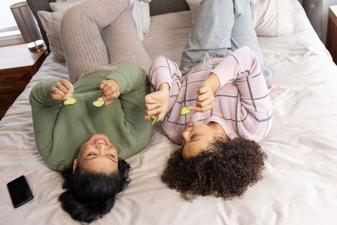 Cozy friends enjoying at-home spa night in pajamas sharing cucumber slices on bed
