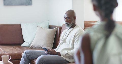 Mature man and younger woman sharing quiet moment in cozy living room, holding smartphone