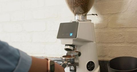 Barista grinding fresh coffee beans into portafilter on modern white espresso grinder countertop