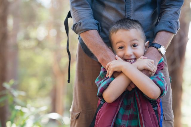 This image captures a joyful moment between a father and his young son in a forest. The boy is smiling and hugging his father, showcasing a strong bond and happiness. Ideal for use in family-oriented advertisements, parenting blogs, outdoor adventure promotions, and articles about father-son relationships.
