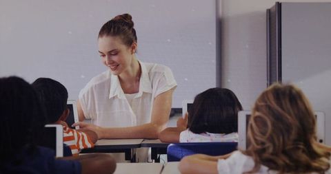 Female teacher helping elementary students with tablets in classroom for collaborative learning