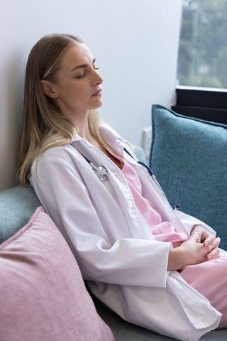 Female nurse resting on sofa in staff lounge wearing pink scrubs and stethoscope