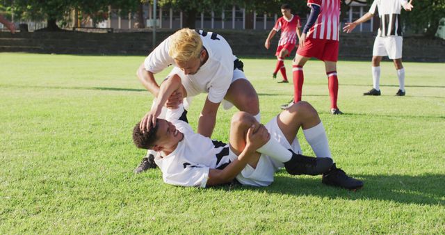 Image of two diverse footballers helping fouled teammate. Male football team, inclusivity and fitness in team sports.