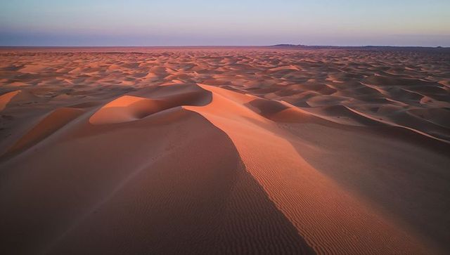 Sunrise casting warm light across rippled sand dunes and long desert horizon