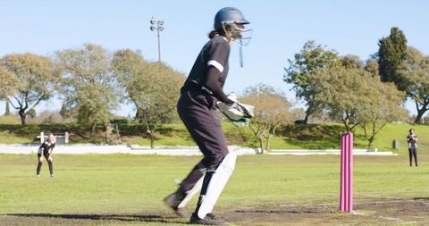 Female cricket team playing on grass pitch with protective gear