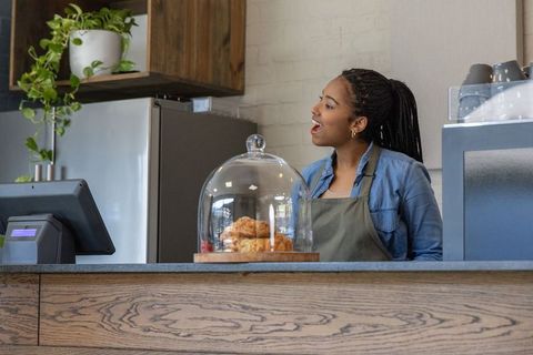 African american barista serving at modern cafe counter with pastries and pos