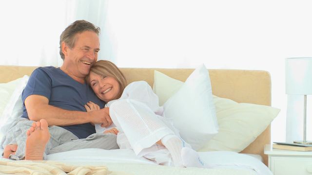 This video depicts a senior couple comfortably sitting on a bed in a bright setting, exuding happiness and love. Ideal for use in content related to healthy aging, relationships, senior living, and retirement lifestyles.