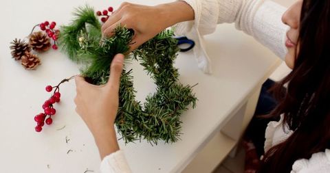 Woman crafting holiday wreath with greenery and berries at home