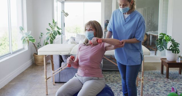 Physical therapist assists elderly woman in rehabilitation exercises at home. Suitable for use in articles or promotional materials related to elderly care, physical therapy, in-home medical services, or showcasing healthcare practices during COVID-19.