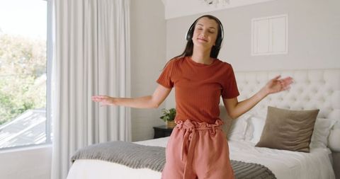 Woman Dancing Joyfully in Bedroom with Headphones for Relaxation