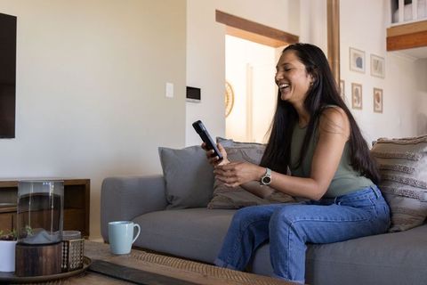 Smiling woman relaxing on sofa using remote control in cozy living room with coffee mug