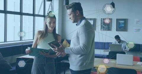 Young coworkers collaborating over tablet and binder in modern open office lounge