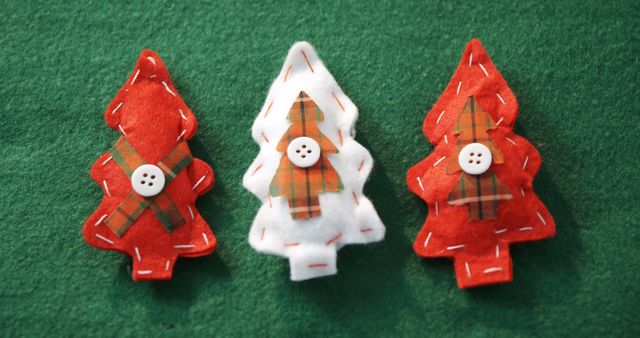 Three handmade Christmas tree decorations are displayed against a green felt background, with copy space. Each ornament features a unique plaid pattern and a small button, adding a cozy, festive touch to the holiday season.