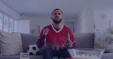 Man in Red Jersey Energized Watching Soccer at Home with Snacks and Beer