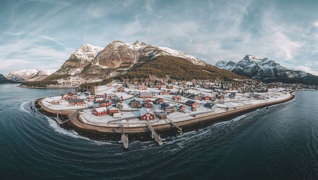 Red coastal cabins featuring snow-covered peninsula, dramatic mountains and twin piers
