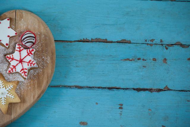 Christmas gingerbread cookies with red and white icing placed on heart-shaped cutting board on rustic blue wooden table. Ideal for holiday greeting cards, festive blog posts, baking websites, and Christmas-themed promotions. Celebrates warmth and joy of the holiday season.