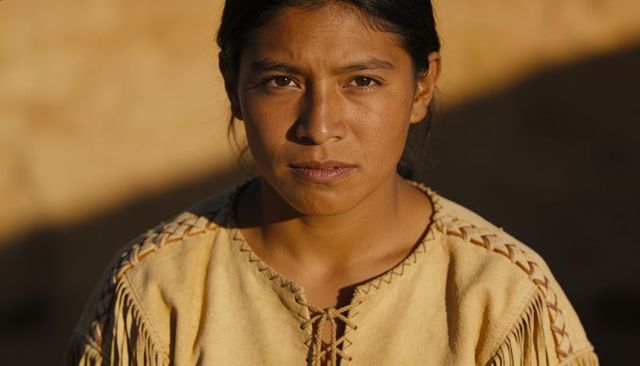 Sunlit hispanic woman wearing fringed suede tunic holding steady gaze in golden hour