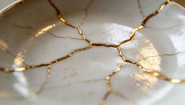 Kintsugi gold-repaired porcelain bowl close-up showing gilded cracklines and warm glow