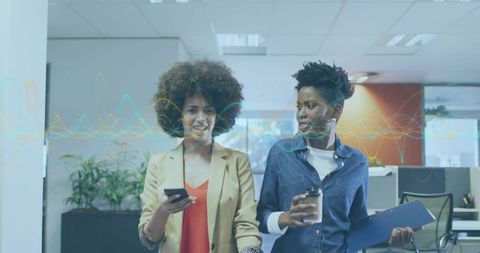 Two professionals walking and chatting in modern open office holding phone, coffee and file