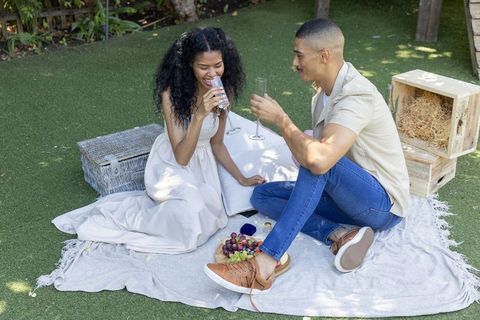 Couple clinking champagne flutes during romantic garden picnic with visible ring box