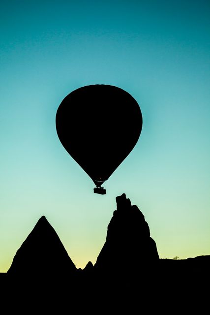Hot air balloon floating high over unique rock formations during sunset, creating a beautiful silhouette against the gradient sky. Perfect for travel and adventure concepts, tourism advertisements, tranquil nature scenes, or illustrating outdoor activities and explorations.