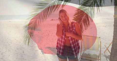 Smiling woman in denim shorts on white sand under palm fronds with striped deck chair