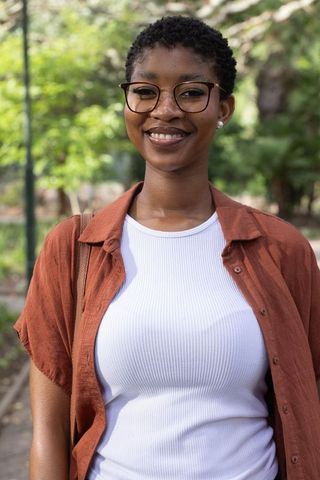 African american young woman smiling in park wearing glasses and casual rust shirt portrait