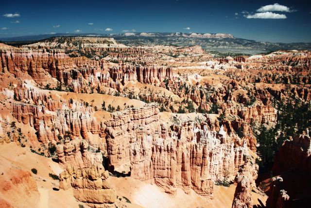 Bryce Canyon National Park features stunning rock formations and is well-known for its unique hoodoos created through erosion. This photo captures the vast expanse and natural beauty of the park under a bright, sunny sky with a scenic view ideal for travel promotions, nature photography collections, and promotional travel content.
