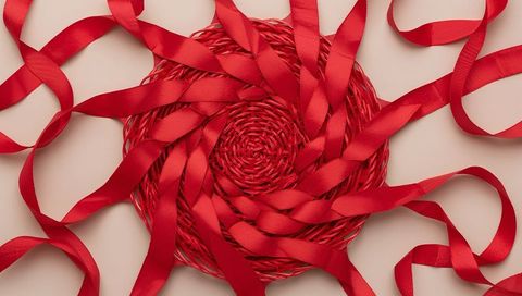 Crimson satin ribbon spiral draped over round woven placemat on pale beige background