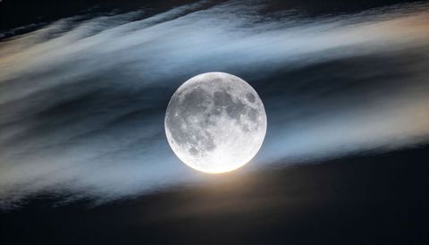 Full moon rising through wispy clouds, casting soft halo and revealing crater detail
