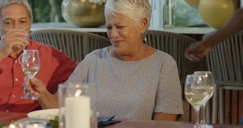 Senior couple celebrating intimate candlelit dinner with wine, balloons and conversation