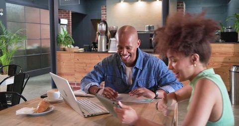 Young professionals collaborating in modern cafe using laptop and tablet, remote teamwork