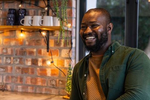 African american man smiling in cozy cafe with exposed brick wall and warm string lights