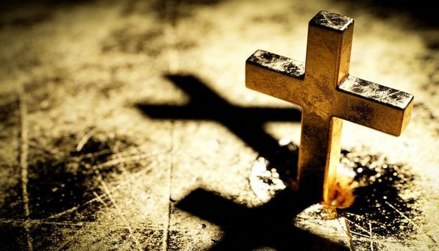 Golden cross standing on scratched surface casting dramatic shadow with wax pool