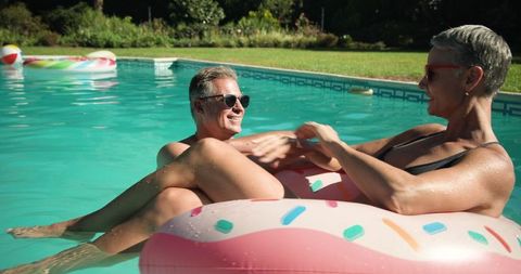 Senior couple relaxing on fun pool floats in serene backyard oasis