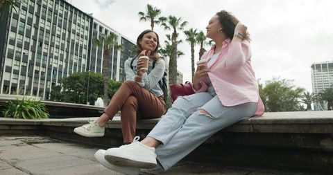 African american friends chatting and enjoying coffee on urban fountain ledge