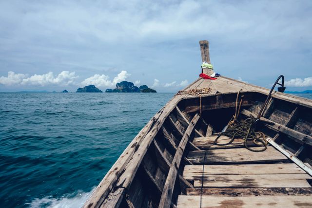 This image depicts a traditional wooden longtail boat navigating through tropical waters with islands visible in the background. It captures the essence of maritime travel and the adventure of discovering hidden island destinations. Ideal for use in travel blogs, tourism brochures, vacation advertisements, and adventure-themed promotions.