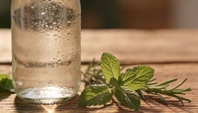 Sunlit glass bottle with condensation, fresh mint and rosemary on rustic wooden table