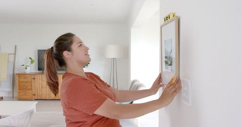 Smiling Woman Hanging Picture Using Spirit Level in Modern Living Room - Download Free Stock Images Pikwizard.com