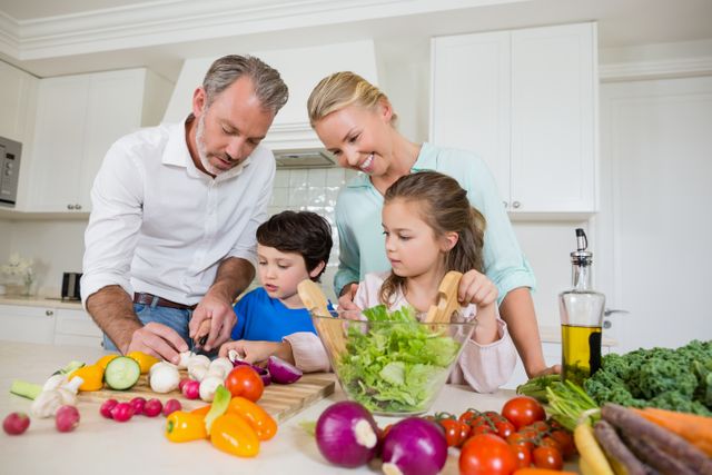 Family preparing a meal together in a bright kitchen. Parents helping children chop vegetables, promoting healthy eating and family bonding. Ideal for use in articles about family activities, healthy lifestyles, and cooking together.